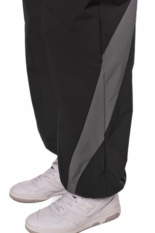 Person trägt Sports Trackpants Black, aus robustem Rip-Stop Gewebe mit OLAKALA Logo, kombiniert mit weißen Sneakers für sportlichen Look.