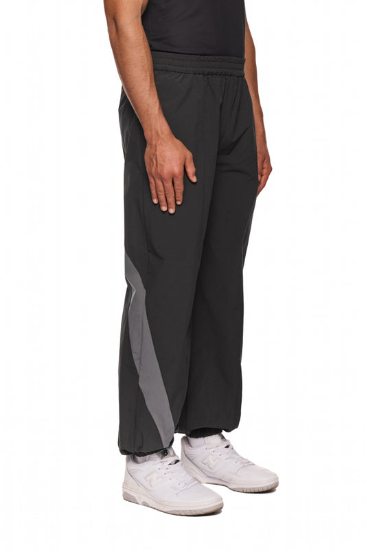 Person trägt schwarze Sports Trackpants mit OLAKALA Sports Logo, elastischem Bund und sportlichen Stoffeinsätzen. Weiße Sneakers sind auch sichtbar.