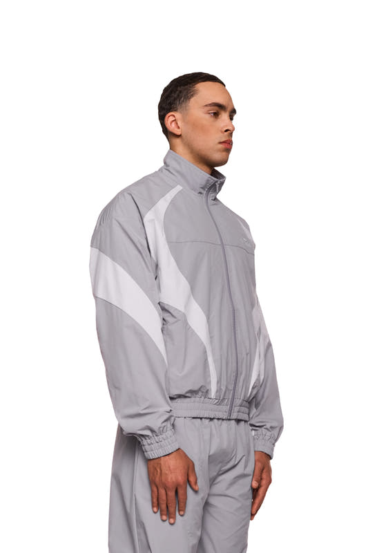 Ein Mann trägt die Sports Trackjacket Gray mit gesticktem OLAKALA Logo, elastischen Bündchen und sportlichen Stoffeinsätzen für eine lockere, komfortable Passform.