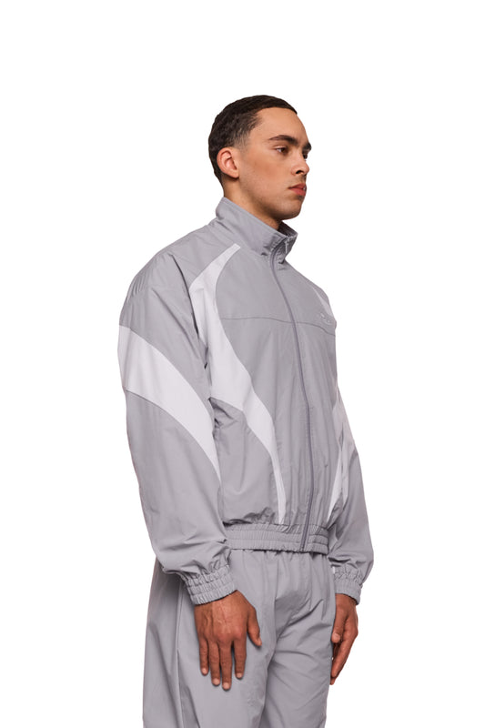 Ein Mann trägt die Sports Trackjacket Gray mit gesticktem OLAKALA Logo, elastischen Bündchen und sportlichen Stoffeinsätzen für eine lockere, komfortable Passform.
