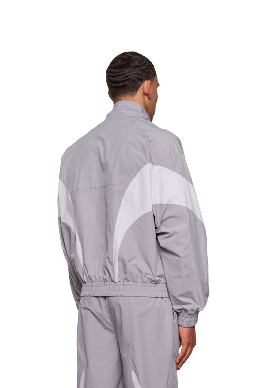 Mann im grauen Sports Trackjacket aus Rip-Stop Gewebe mit gesticktem OLAKALA Logo, sportlicher Look durch kontrastfarbene Einsätze und elastische Bündchen.