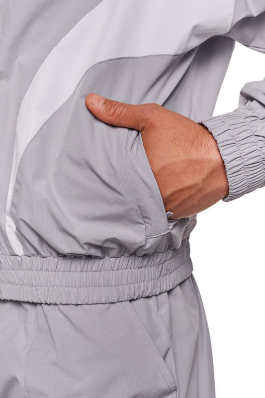 Person trägt eine graue Sports Trackjacket von OLAKALA mit gesticktem Logo, elastischen Bündchen und kontrastfarbenen Einsätzen für sportlichen Look.