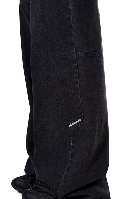 Nahaufnahme der CC Black Denim Pants Baggy mit versetzter Seitennaht, gesticktem OLAKALA-Logo und „Mittelfinger“-Patch auf der vorderen Gürtelschlaufe.