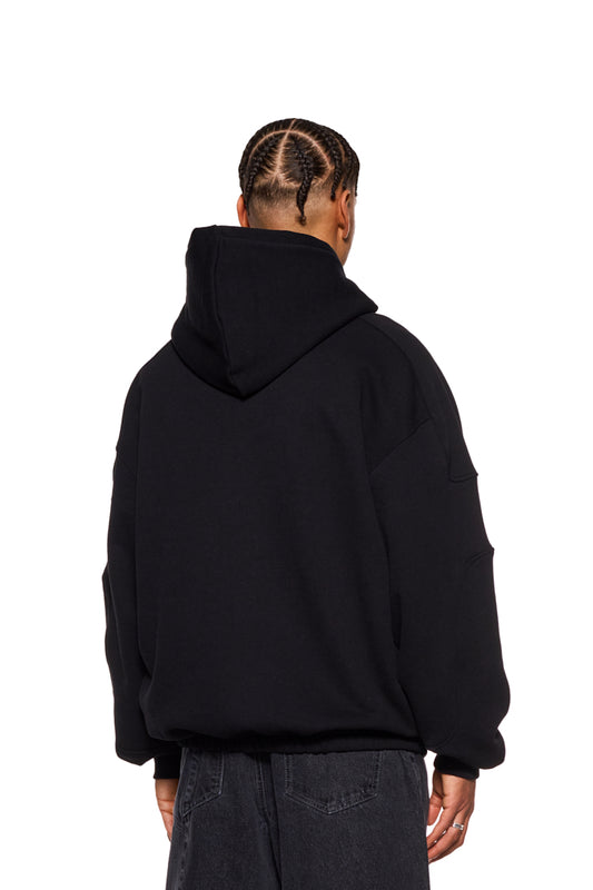 Person wears the CC Hoodie Black with an embroidered OLAKALA logo on the chest, dividing seams on the sleeves and an elasticated hem in an oversized fit.