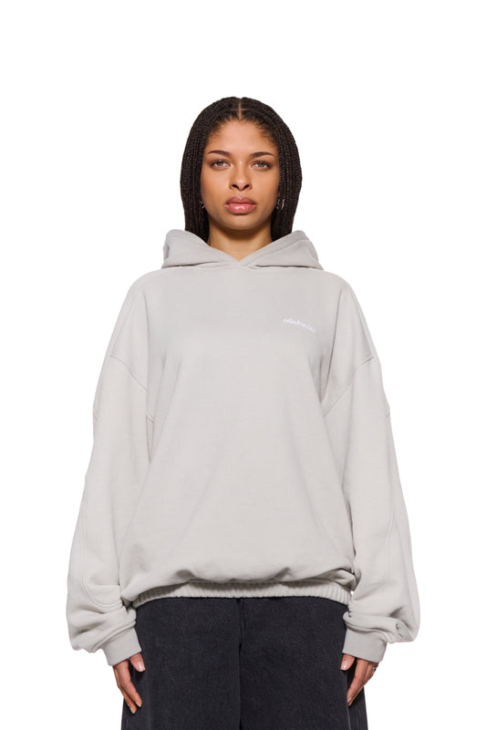 Woman wears CC Hoodie Pussywillow Gray with dividing seams, ribbed cuffs and embroidered OLAKALA logo on the chest, oversized and unisex.