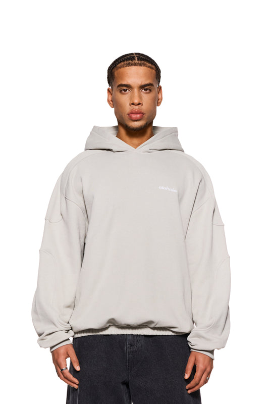 Mann trägt CC Hoodie Pussywillow Gray mit Teilungsnähten, Ripp-Bündchen und gesticktem OLAKALA Logo, zeigt oversized Passform und unisex Design.