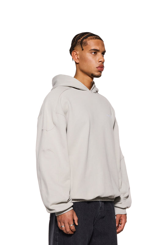 Mann in grauem CC Hoodie Pussywillow mit gesticktem OLAKALA Logo und Teilungsnähten an Ärmeln, zeigt Oversized-Passform.