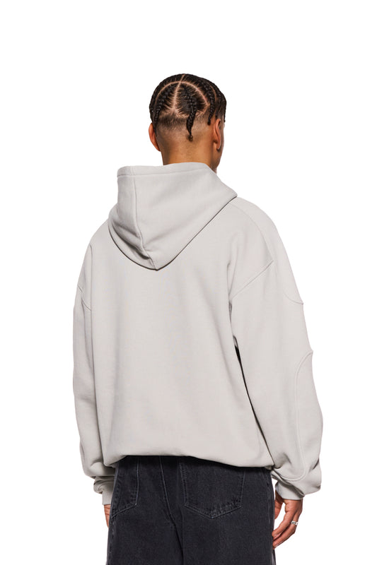 Person wears CC Hoodie Pussywillow Gray with embroidered OLAKALA logo on the chest, dividing seams and ribbed cuffs. Oversized, unisex design.