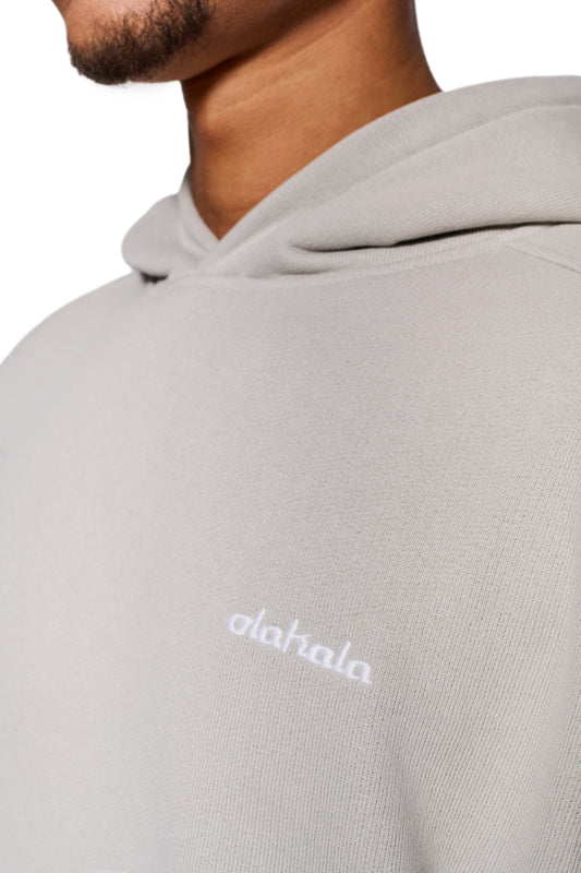 Person wearing CC Hoodie Pussywillow Gray with dividing seams, ribbed cuffs and embroidered OLAKALA logo, oversized unisex fit.