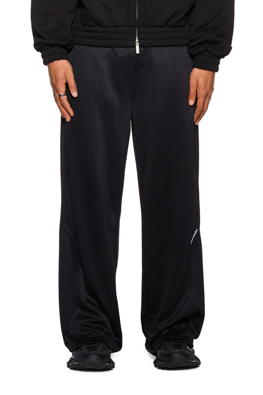 Person trägt CC Jogger Pants Black mit elastischem Bund und französischen Eingriffstaschen, gesticktem OLAKALA Logo, lockerer Passform und versetzter Seitennaht.