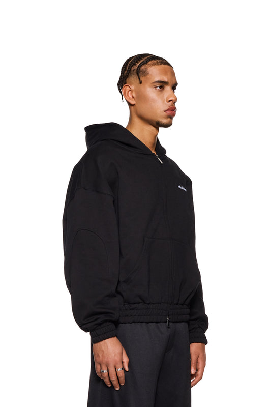 Mann trägt CC Zip Hoodie Schwarz mit gesticktem OLAKALA Logo, 2-Wege-Reißverschluss und elastischen Bündchen, oversized und unisex.