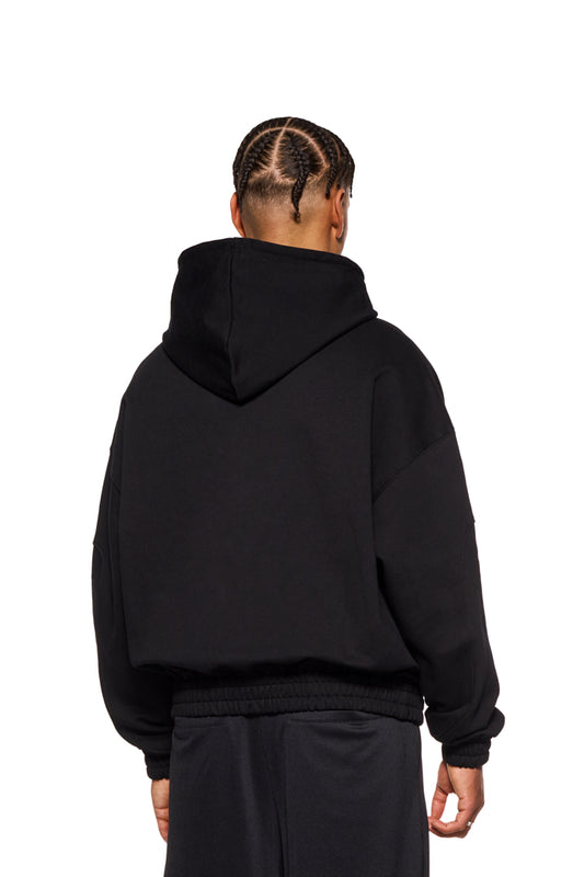 Person trägt CC Zip Hoodie Black mit gesticktem OLAKALA-Logo, elastischen Bündchen und Oversized-Passform, zeigt Rückansicht und Nahaufnahme der Tasche.