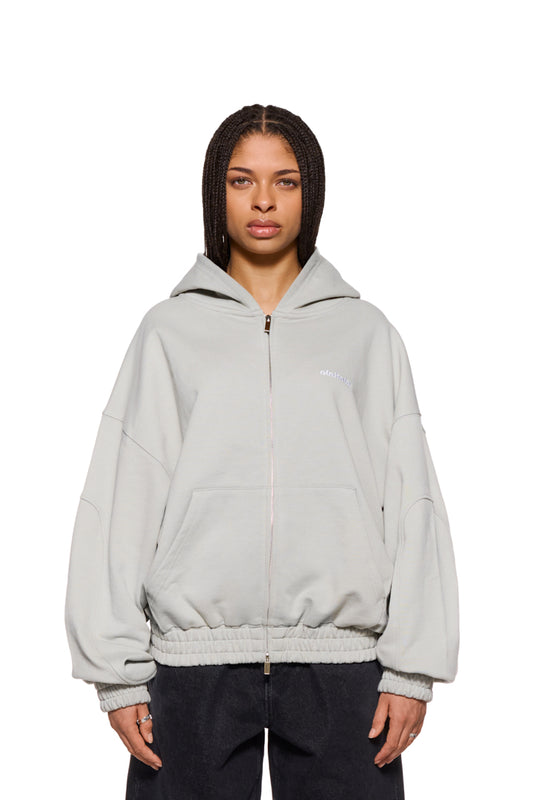 Frau trägt CC Zip Hoodie Pussywillow Gray mit gesticktem OLAKALA-Logo, elastischen Bündchen und 2-Wege-Reißverschluss. Oversized Unisex-Passform.