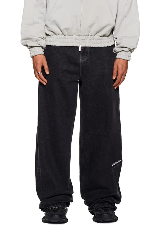 Person trägt CC Black Loose Fit Denim Pants mit versetztem Bund und OLAKALA-Logo, zeigt lockeren Unisex-Schnitt und 5-Pocket-Design.