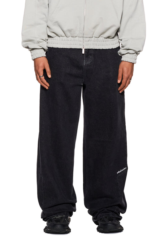 Person trägt CC Black Loose Fit Denim Pants mit versetztem Bund und OLAKALA-Logo, zeigt lockeren Unisex-Schnitt und 5-Pocket-Design.