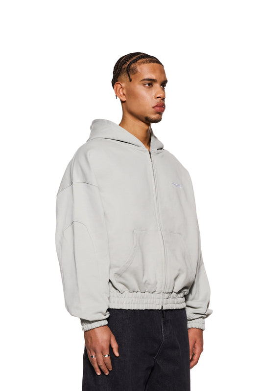 Mann trägt CC Zip Hoodie Pussywillow Gray mit Reißverschluss und gesticktem OLAKALA Logo, betont durch Oversized-Passform und elastische Bündchen.