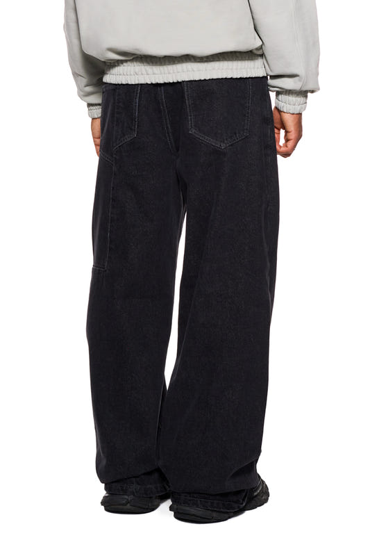 Person trägt CC Black Loose Fit Denim Pants mit versetztem Hosenbund, 5 Taschen, gesticktem OLAKALA Logo und geprägtem Patch, lockere Passform.