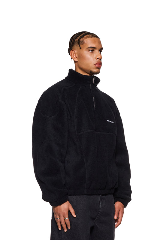 Mann im CC Fleece Halfzip Black mit hohem Kragen und gesticktem OLAKALA Logo, zeigt elastische Bündchen und Reißverschluss.
