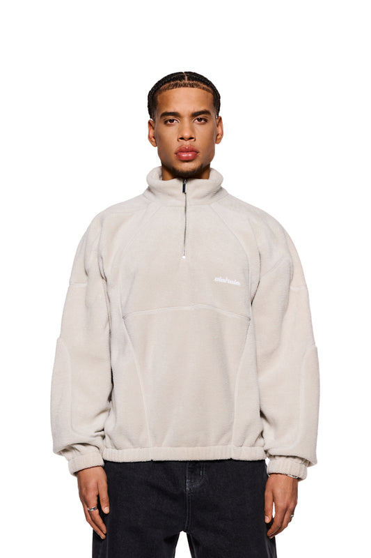 Mann in weißer Jacke, CC Fleece Halfzip Pussywillow Gray mit elastischen Bündchen, hohem Kragen und gesticktem OLAKALA Logo auf der Brust. Oversized Fit.
