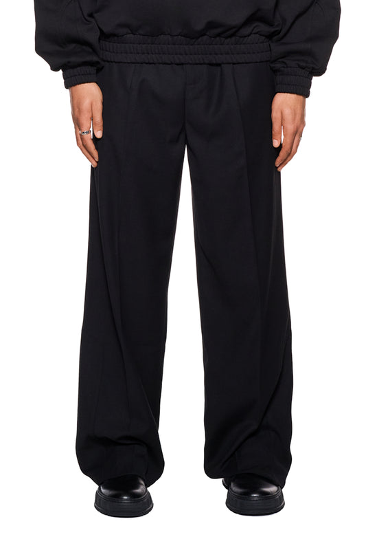 Person trägt CC Dress Pants Loose Fit mit asymmetrischen französischen Taschen und gesticktem OLAKALA Logo, lockere Passform, ideal für vielseitige Unisex-Styles.