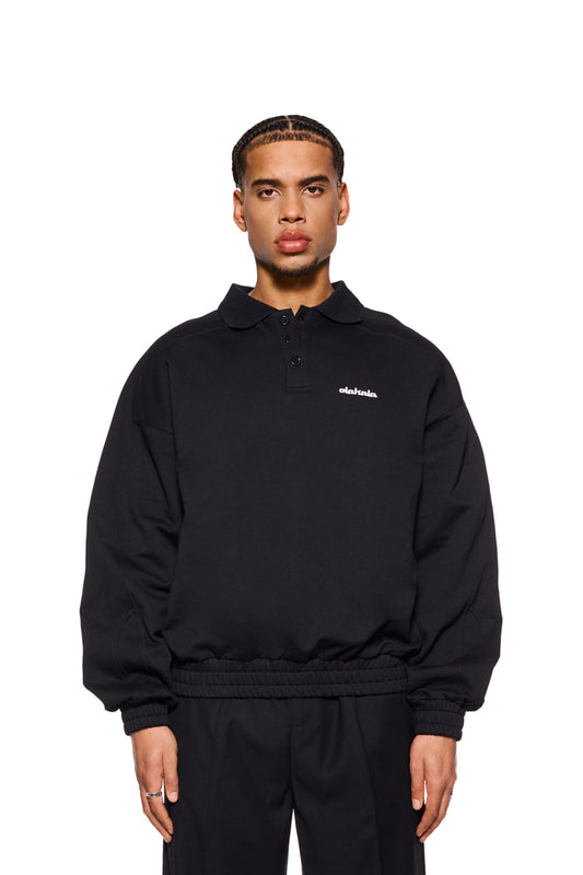 Mann trägt das CC Polo Longsleeve Black mit Polokragen, Knopfleiste und gesticktem OLAKALA Logo auf der Brust. Oversized Passform, unisex Design.