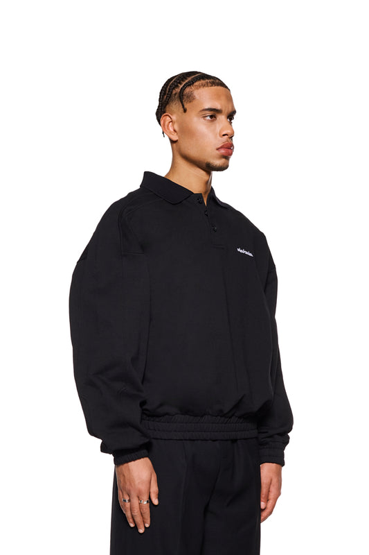 Mann trägt CC Polo Longsleeve Black mit Polo-Kragen, Knopfleiste und gesticktem OLAKALA Logo, oversized Passform und elastischen Bündchen.