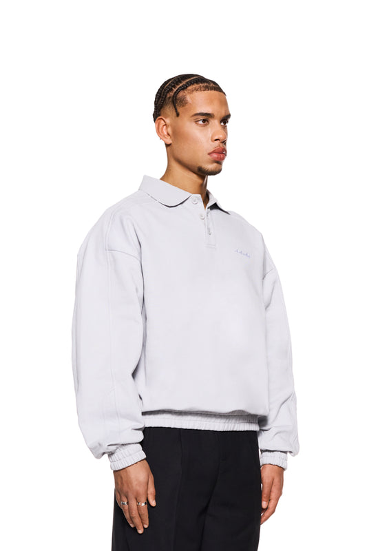 Mann trägt CC Polo Longsleeve Gray mit Polo-Kragen, Knopfleiste und gesticktem OLAKALA Logo, präsentiert oversized Unisex-Stil.