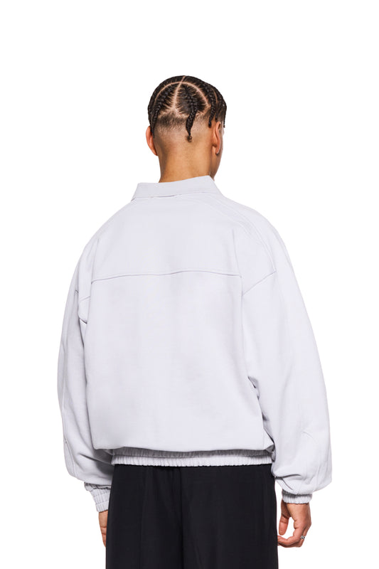 Person mit Zöpfen trägt CC Polo Longsleeve Gray mit Polokragen, Knopfleiste und gesticktem OLAKALA-Logo auf der Brust. Oversized Passform, unisex Design.