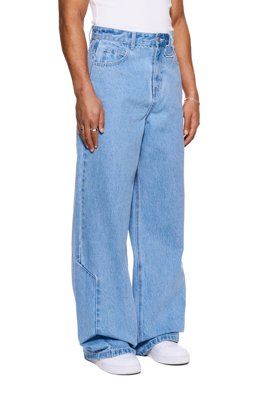 Person wears CC Blue Loose Fit Denim Pants with offset waistband and embroidered OLAKALA logo, combined with white shoes. Loose fit, unisex design.
