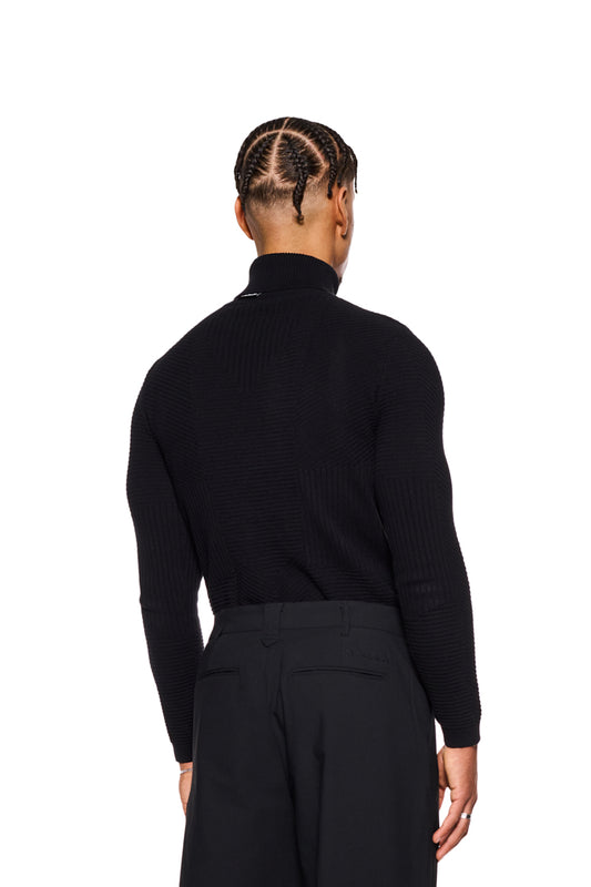 Mann trägt schwarzen Anatomy Rollkragenpullover von OLAKALA mit verschiedenen Strickmustern und engem Schnitt, sichtbar ist das OLAKALA-Tag am Kragen.