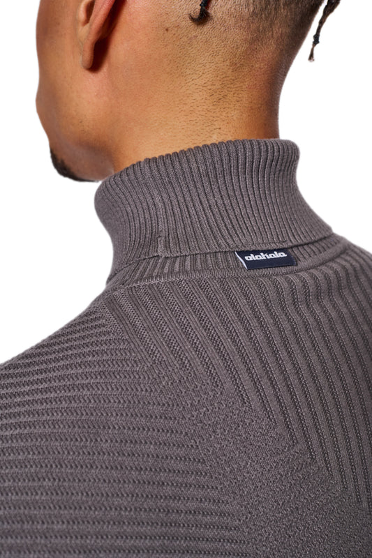 Person trägt den Anatomy Turtleneck Gray mit Rollkragen und OLAKALA-Label am Kragen, betont durch eng anliegende Passform und verschiedene Strickmuster.