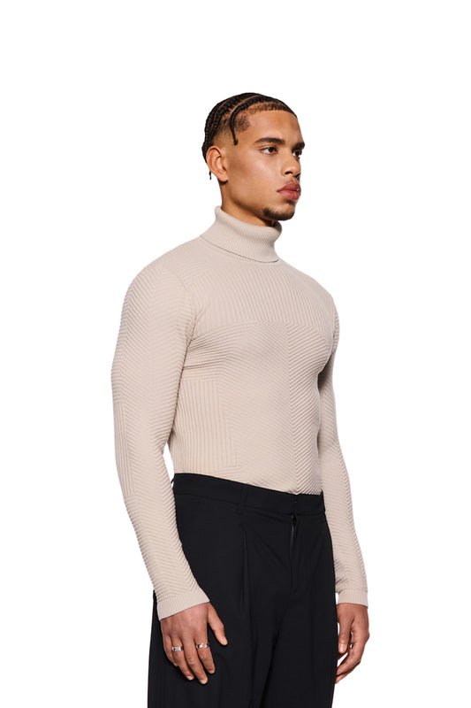 Mann trägt Anatomy Turtleneck Beige mit Rollkragen, eng anliegendem Schnitt und OLAKALA-Tag am Kragen, kombiniert mit schwarzer Hose und Ringen.