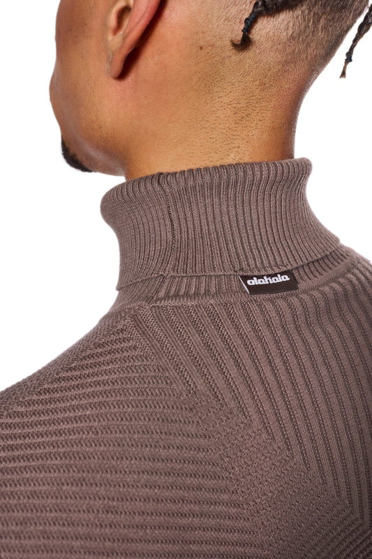 Anatomy Turtleneck Brown: Person trägt einen eng anliegenden, gestrickten Rollkragenpullover mit OLAKALA-Logo am Kragen, passend für Unisex-Kleidung.