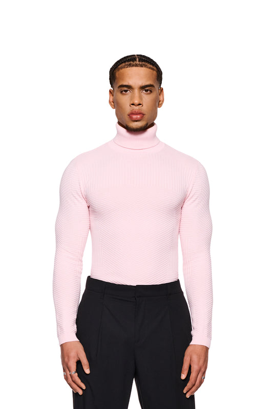 Mann trägt den Anatomy Turtleneck Pink, einen eng anliegenden Strickpullover mit Rollkragen und OLAKALA-Tag am Kragen, kombiniert mit schwarzen Hosen.
