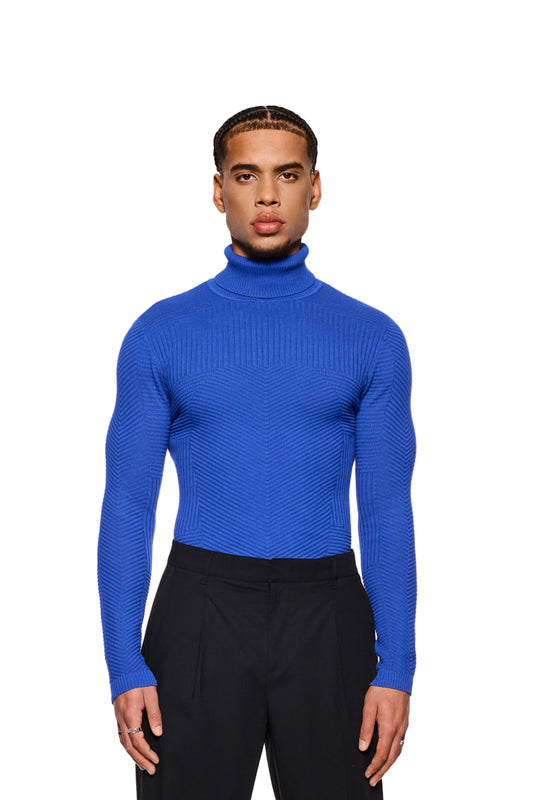 Mann trägt Anatomy Turtleneck Blue mit Rollkragen und enger Passform, Teil der OLAKALA-Kollektion, zeigt Strickmuster und OLAKALA-Tag am Kragen.