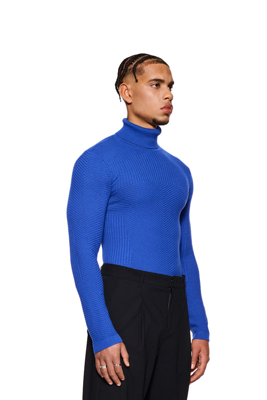 Mann trägt ein blaues Anatomy Turtleneck von OLAKALA mit Rollkragen und enganliegender Passform, verziert mit OLAKALA-Tag am Kragen.