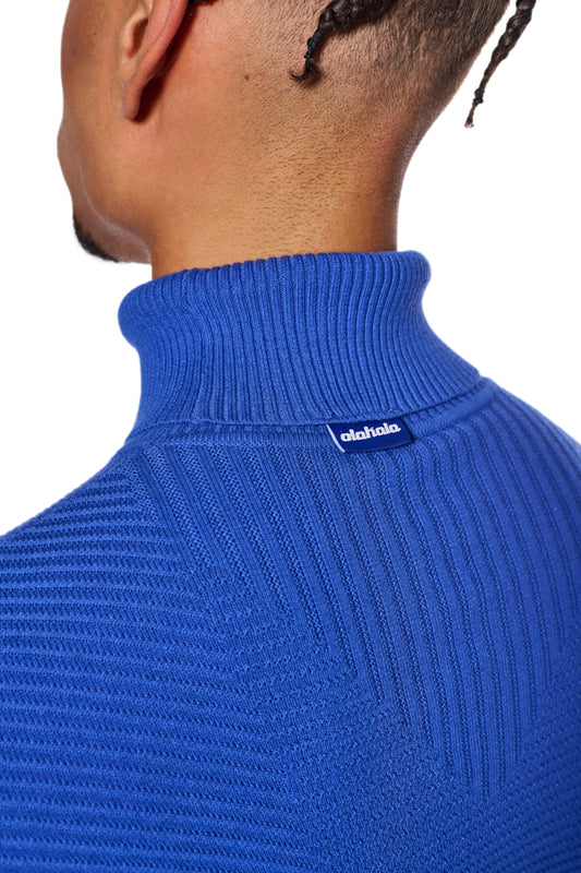 Person trägt den Anatomy Turtleneck Blue mit Rollkragen und OLAKALA-Label, zeigt eng anliegende Passform und verschiedene Strickmuster.