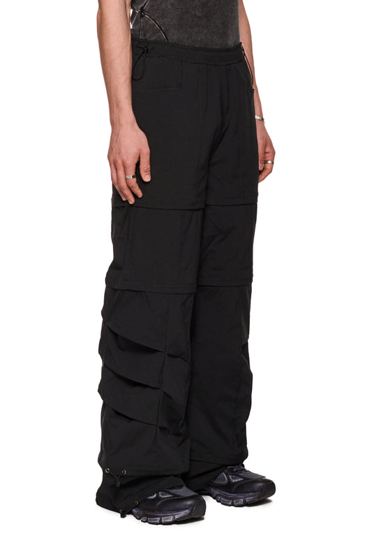 Person trägt Gills Zip-Off Pants Black mit abnehmbaren Hosenbeinteilen, Kiemen-Lufteinlässen und gesticktem OLAKALA-Logo. Robustes Rip-Stop Gewebe, lockere Passform.