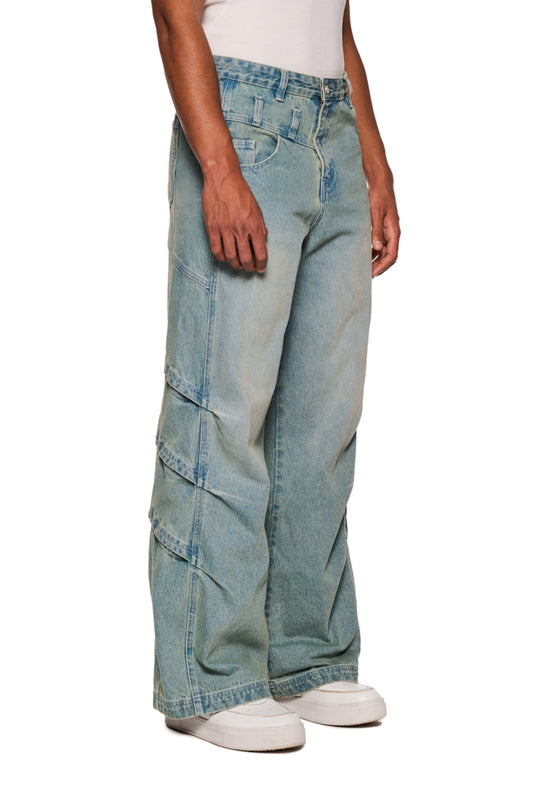 Person trägt Gills Washed Denim Pants Blue mit seitlichen Lufteinlässen und Mittelfinger-Patch, lockere Passform, gesticktes OLAKALA-Logo sichtbar.