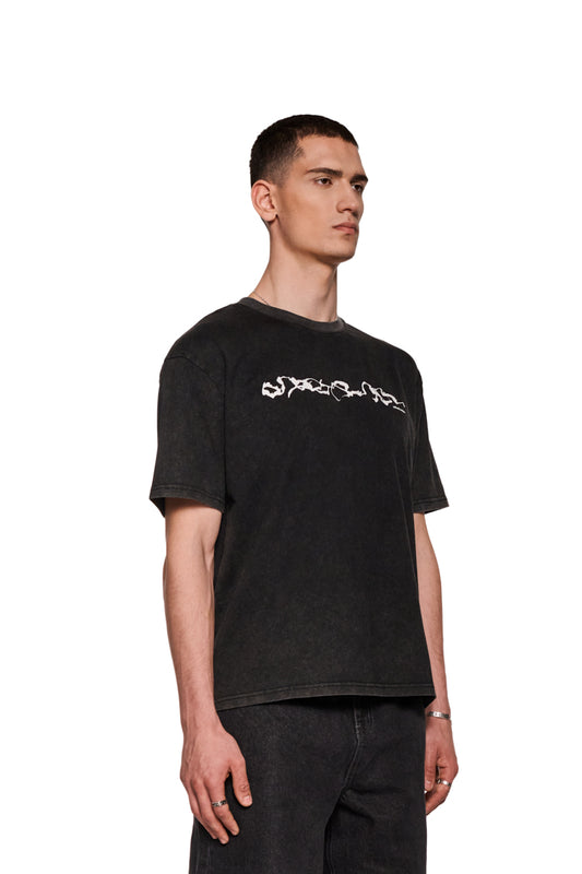Mann trägt E.O.I. T-Shirt in Schwarz mit Siebdruck-Grafik und Ripp-Kragen, zeigt eine entspannte, modische Passform.