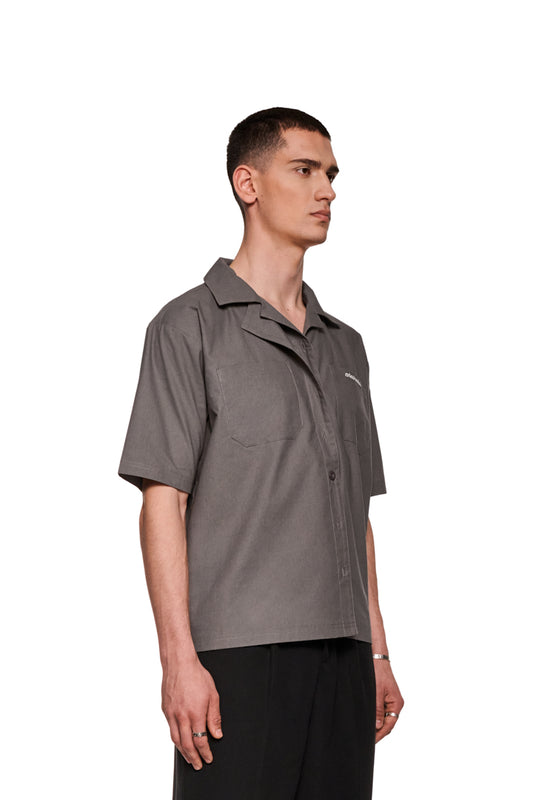 Mann im grauen Layered Short Sleeve Shirt mit kubanischem Kragen und Brusttaschen, gesticktes OLAKALA Logo sichtbar, lockere Passform.
