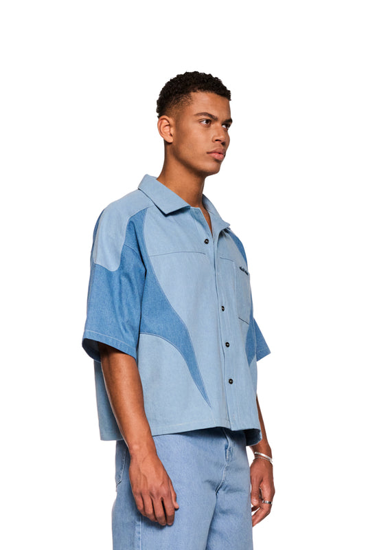 Mann trägt Echoes Denim Shirt mit kubanischem Kragen, Knopfleiste und Brusttasche mit OLAKALA-Logo. Lockerer Schnitt und robuste Köper-Gewebe.
