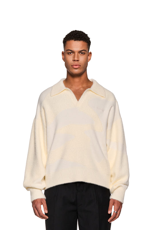 Mann trägt weißen Glitched Fuzzy Polo Cream mit Polo-Kragen, knopfloser Leiste und gesticktem Synergy-Logo auf der Brust; flauschiges Material, unisex.