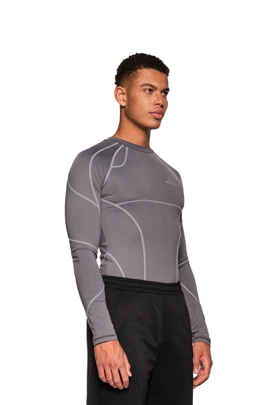 Mann im grauen Sports Anatomy Tech Top mit OLAKALA-Logo auf der Brust, eng anliegendes Design, präsentiert Longsleeve-Details und sportliche Eleganz.