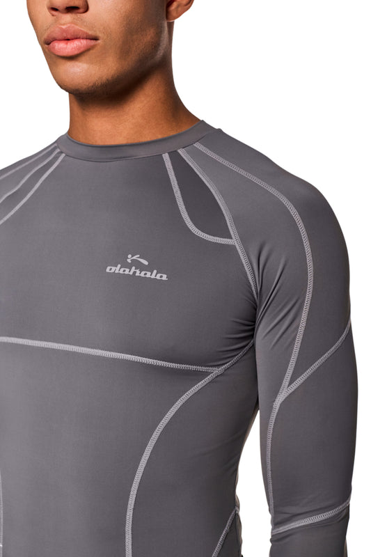 Mann trägt eng anliegendes Sports Anatomy Tech Top Dunkelgrau mit OLAKALA Logo auf der Brust und Ziernähten am Longsleeve.