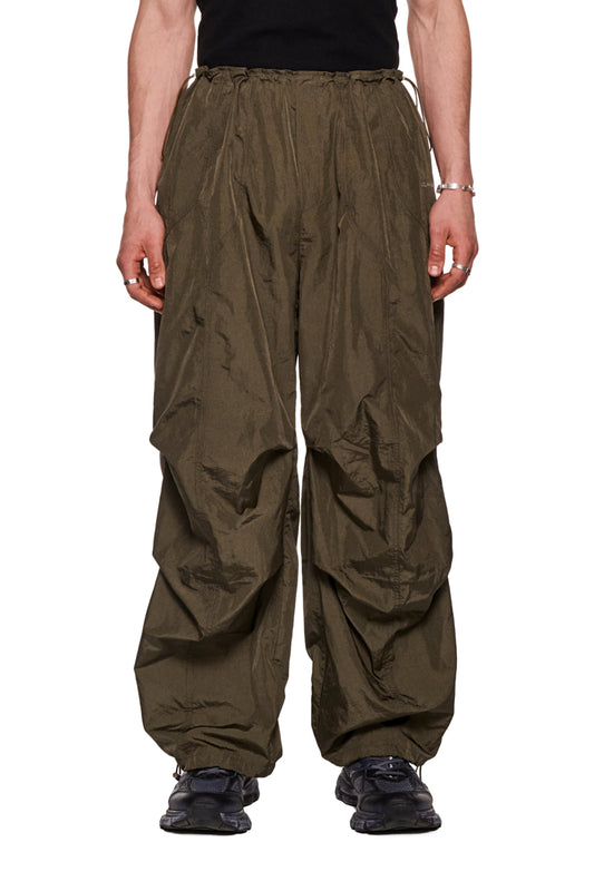 Person trägt Parachute Pants Khaki mit elastischem Kordelzug und gesticktem Synergy-Logo, lockerer Passform und strapazierfähigem Material.