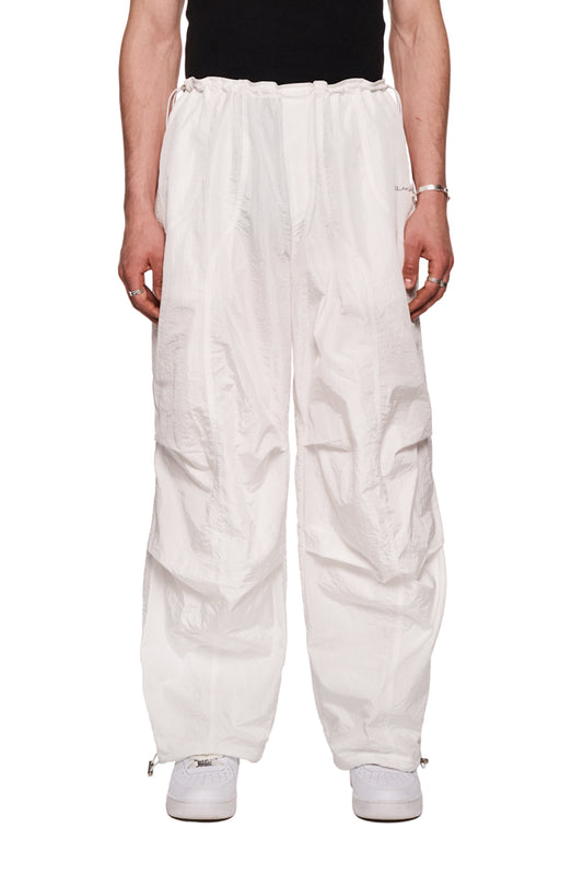 Person trägt OLAKALA Parachute Pants Weiß mit Eingriffstaschen, Paspeltasche, elastischem Kordelzug und gesticktem Synergy-Logo, lockere Passform, strapazierfähig.