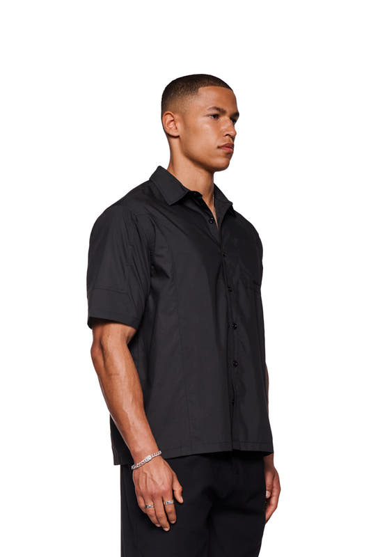 Man wears CC short sleeve shirt black with OLAKALA logo embroidery on chest pocket, button placket and loose fit.
