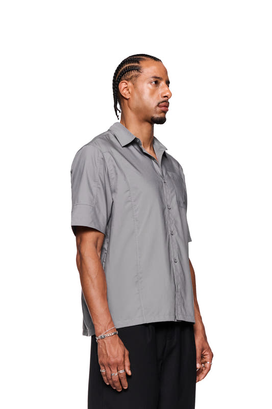 Man with braided hair wearing CC short sleeve shirt gray, showing OLAKALA logo embroidery and silver rings.