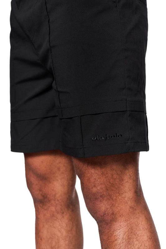 Nahaufnahme von Herrenbeinen in OLAKALA Track Shorts Black mit elastischem Bund, Eingriffstaschen und gesticktem Logo, ideal für Alltag und als Badehose.